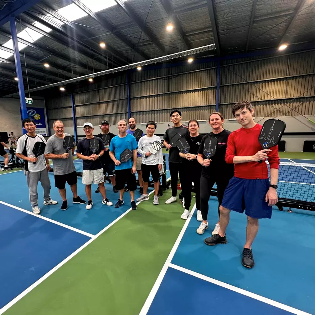 A group gathered on court at Auckland Pickleball Centre, paddles in hand
