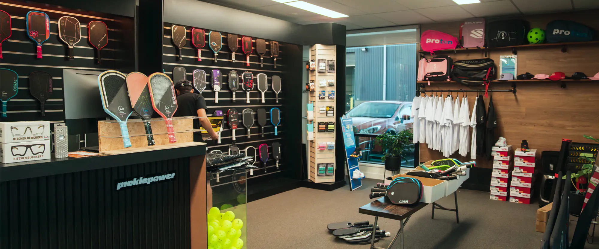 Inside the Picklepower store at Auckland Pickleball Centre, paddles displayed along the wall behind the counter